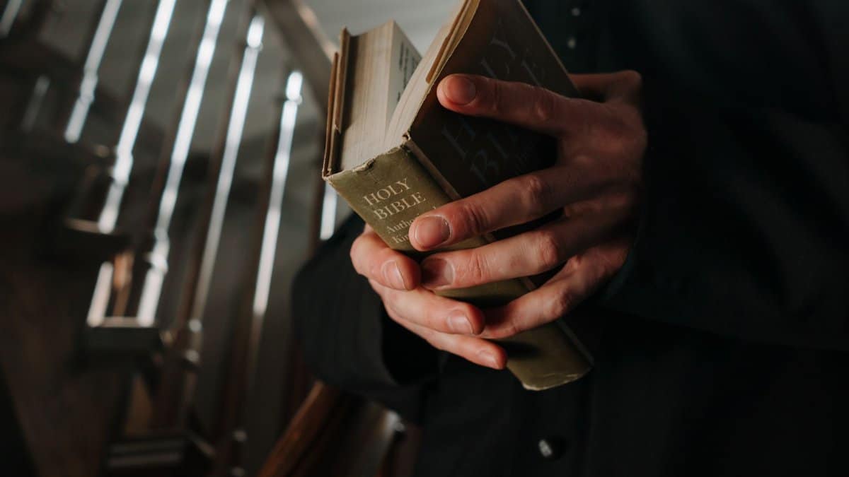 Close-up view of adult hands holding a Holy Bible on a staircase, symbolizing faith and spirituality.