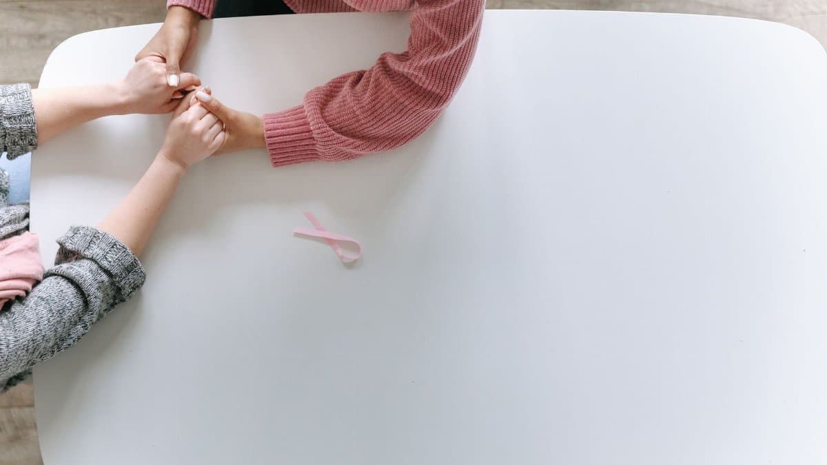 Hands holding in support with a pink ribbon symbolizing breast cancer awareness.