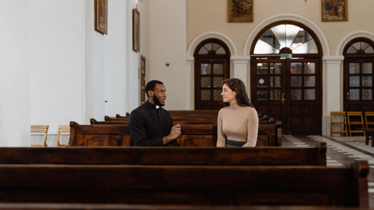 A priest and a woman having a meaningful conversation in a church pew, emphasizing faith and connection.