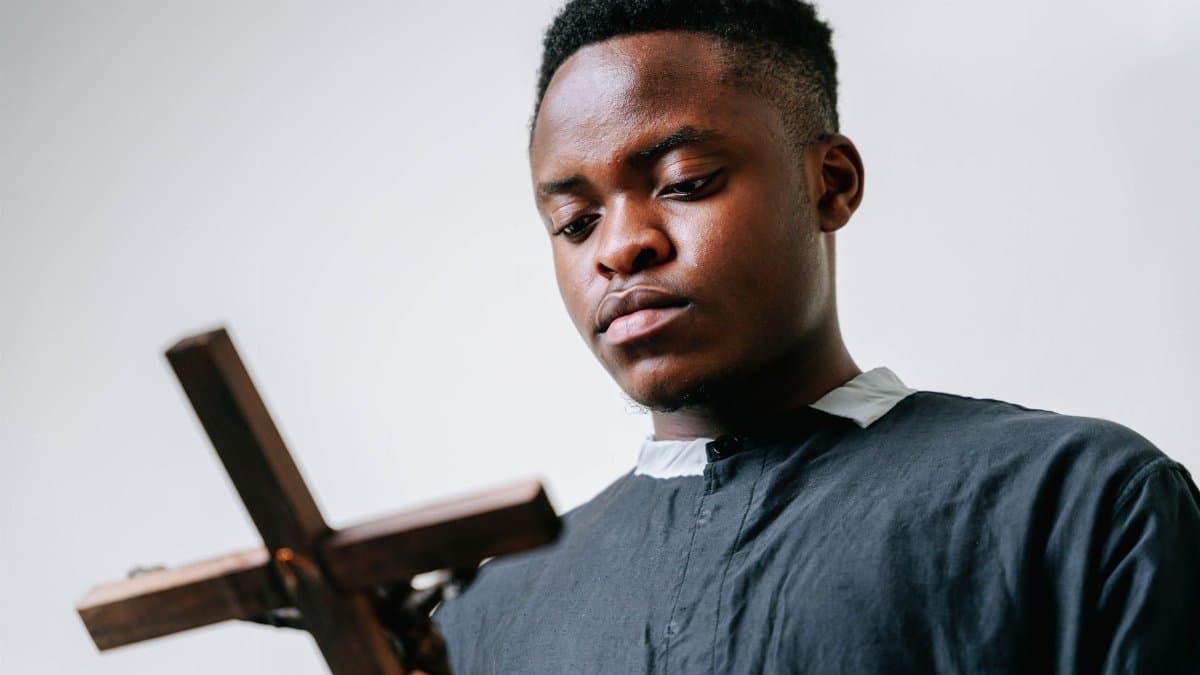 Portrait of an adult man in a cassock holding a wooden cross, symbolizing faith.