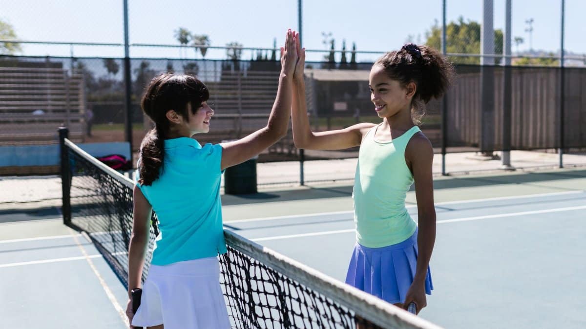 Two teenage girls exchange a high five on a tennis court, capturing the joy of sports and friendship.