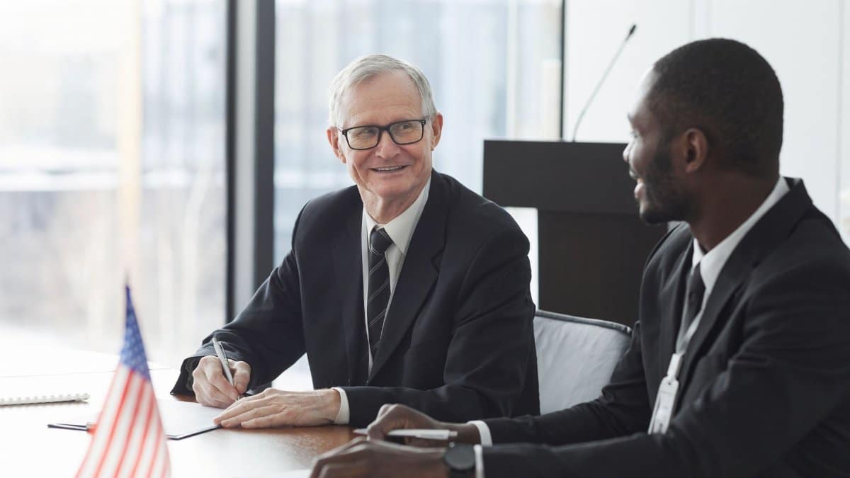 Two business professionals discussing and signing documents at a meeting with an American flag on the table.