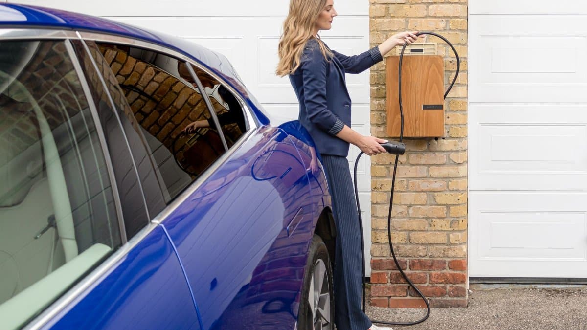 A woman efficiently charges her blue electric car at a home EV charging station.