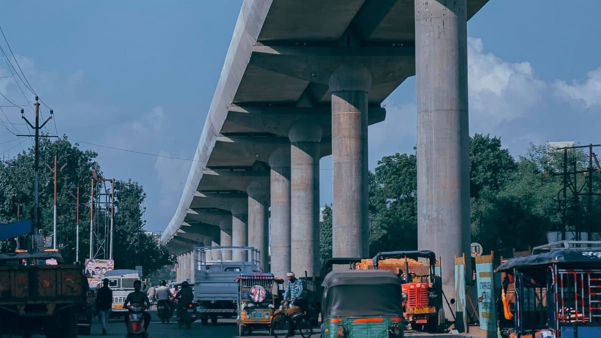 Traffic flows beneath a towering viaduct in a busy urban area, showcasing diverse vehicles.