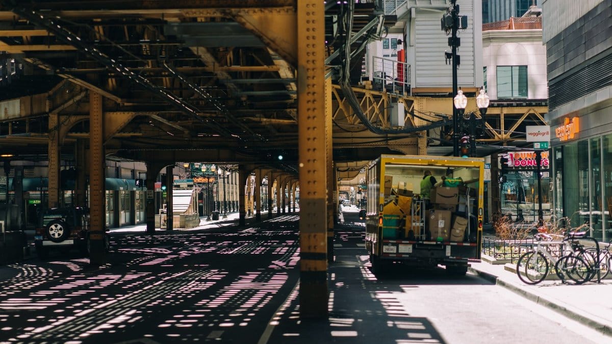 A busy Chicago street under elevated tracks with a delivery truck and bicycles, showcasing urban life.