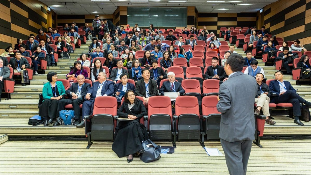 Professional setting of a business conference with attendees and a presenter in an auditorium.