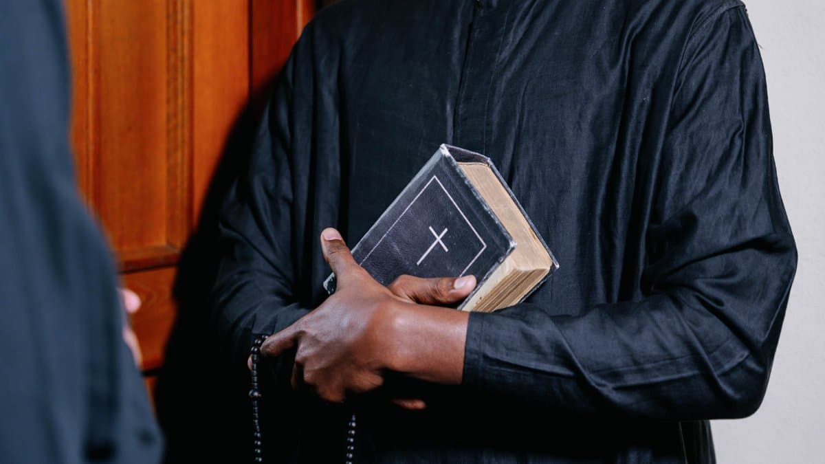 Close-up of a priest holding a Bible and rosary beads, symbolizing faith and spirituality.