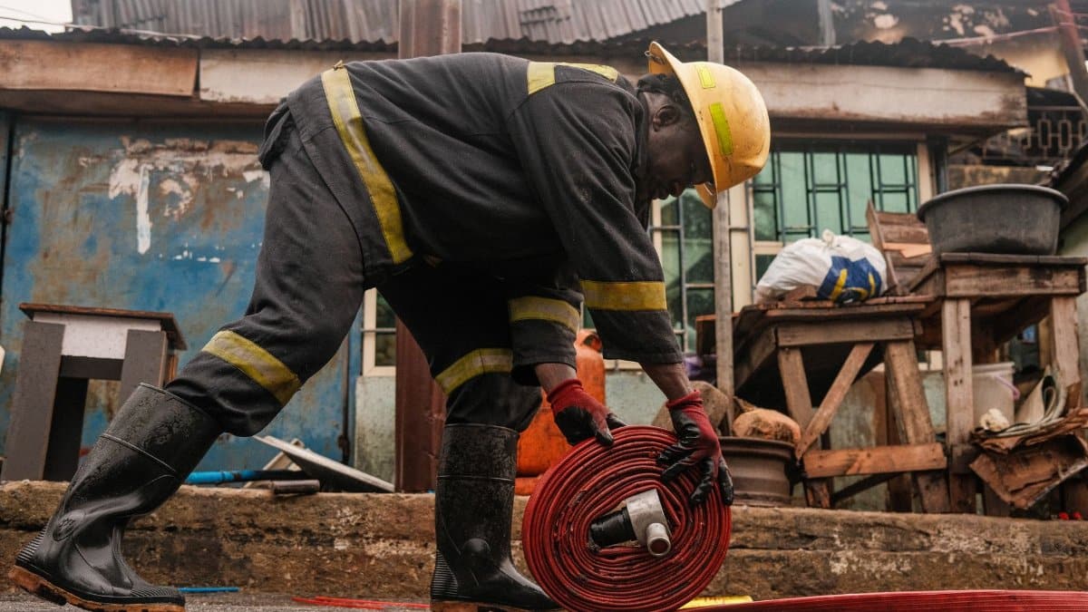 An African firefighter rolls up a fire hose in a Lagos neighborhood post-emergency.