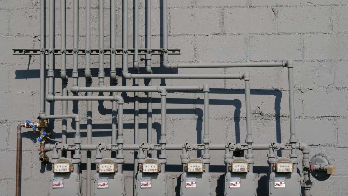 Row of gas meters and piping mounted on a concrete wall, illustrating urban utilities.