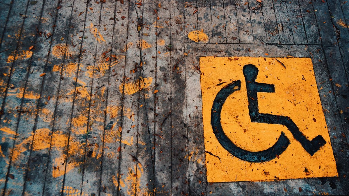 Yellow wheelchair accessibility sign painted on urban pavement with leaves.