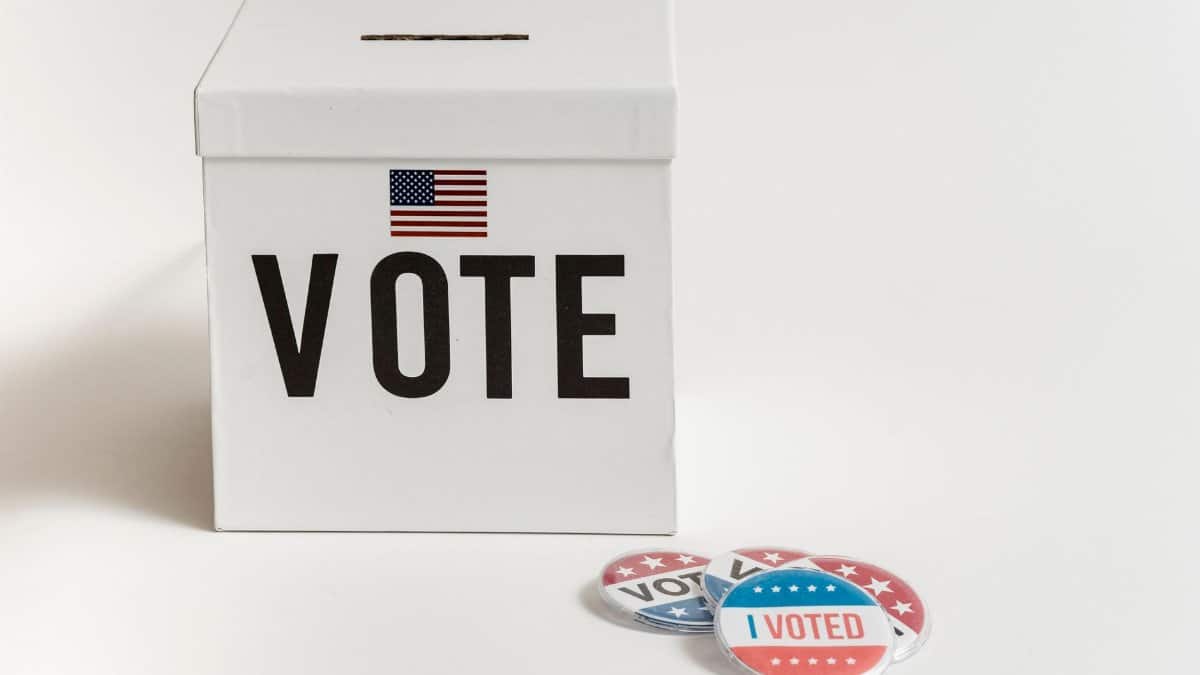White ballot box with USA flag and 'I Voted' badges on a white background.