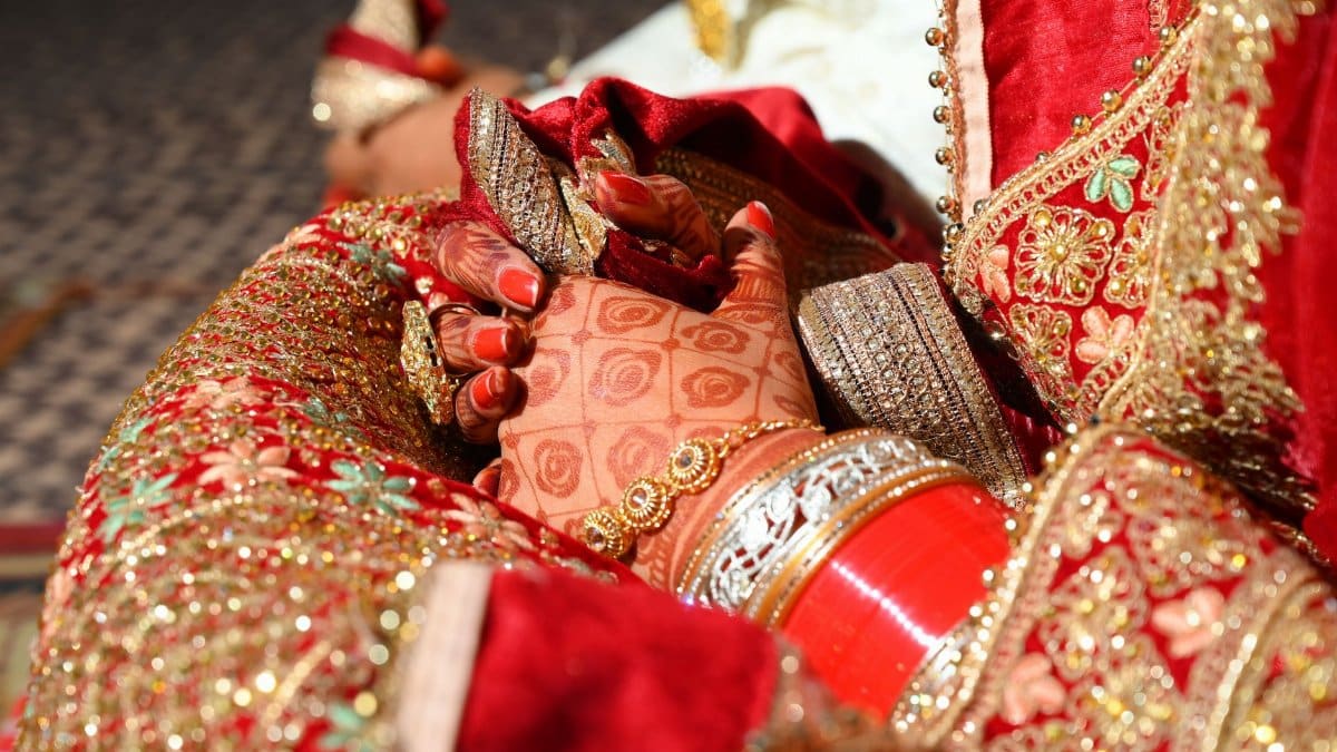 A close-up of an Indian bride's hands with henna tattoos and elegant jewelry, showcasing traditional attire.
