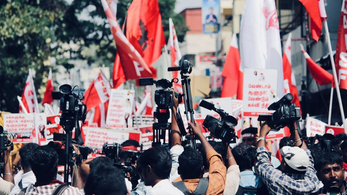 A vibrant protest in Chennai, India with media coverage featuring bright red flags and banners.