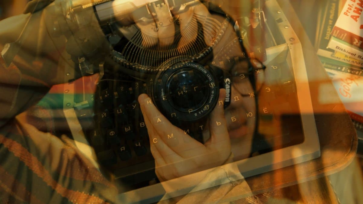 Artistic double exposure featuring a vintage typewriter and a photographer with a camera.