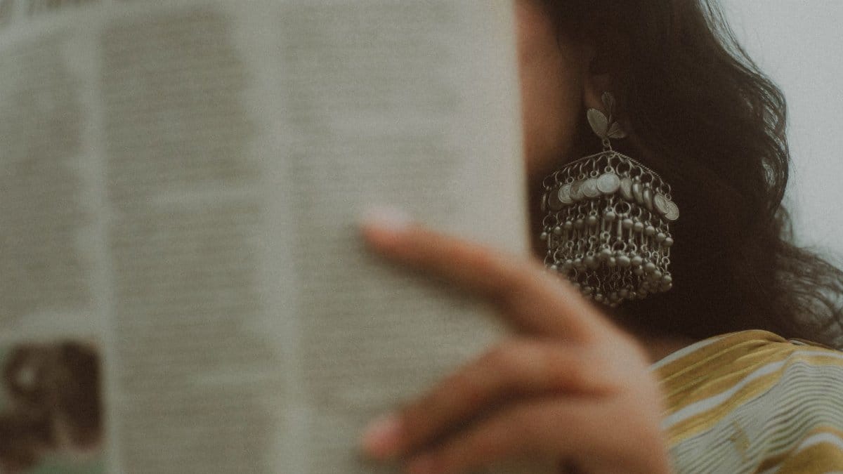 Woman reading a newspaper, showcasing vintage style earrings, creating an artistic and classic mood.