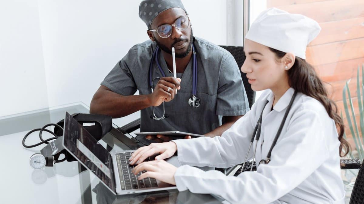 Two doctors discuss patient diagnosis using laptop in hospital office.