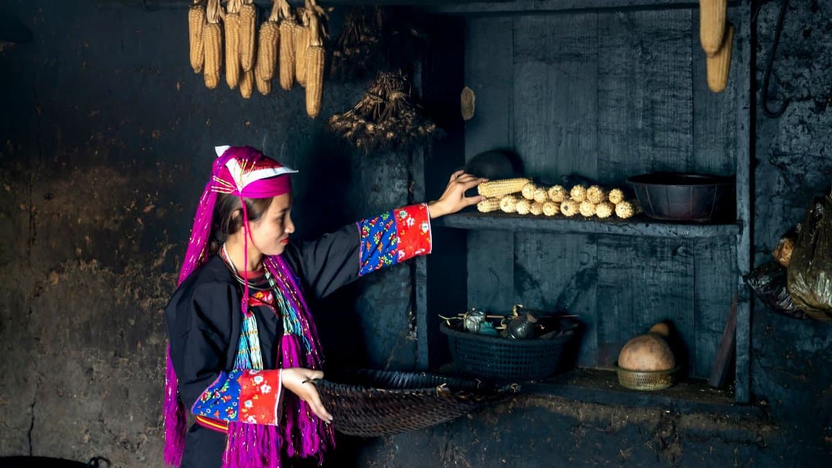 A woman in traditional attire stores corn indoors, capturing cultural heritage and domestic life.