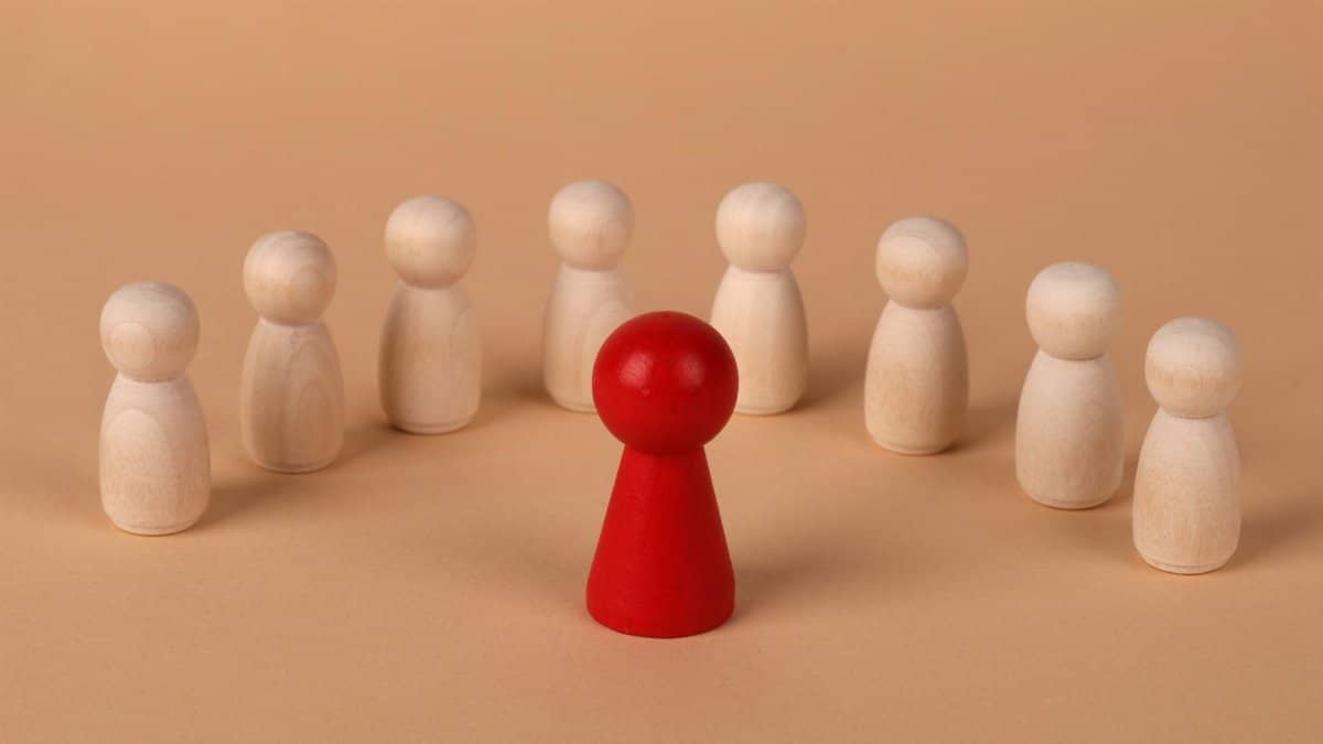 Central red wooden figure surrounded by beige figures symbolizing leadership and individuality.
