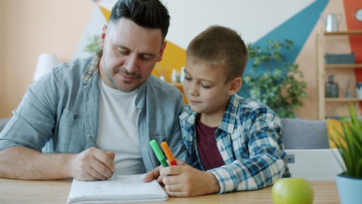 A father and son working on a homework assignment together at home in a colorful setting.