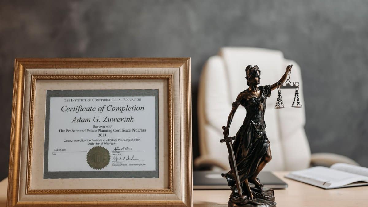 A framed legal certificate and Lady Justice figurine on a desk in a law office setting.