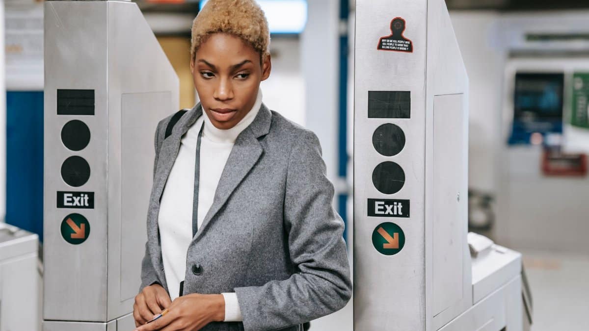 Serious young African American female entrepreneur with short hair and in elegant outfit walking through automatic turnstile machine in subway station