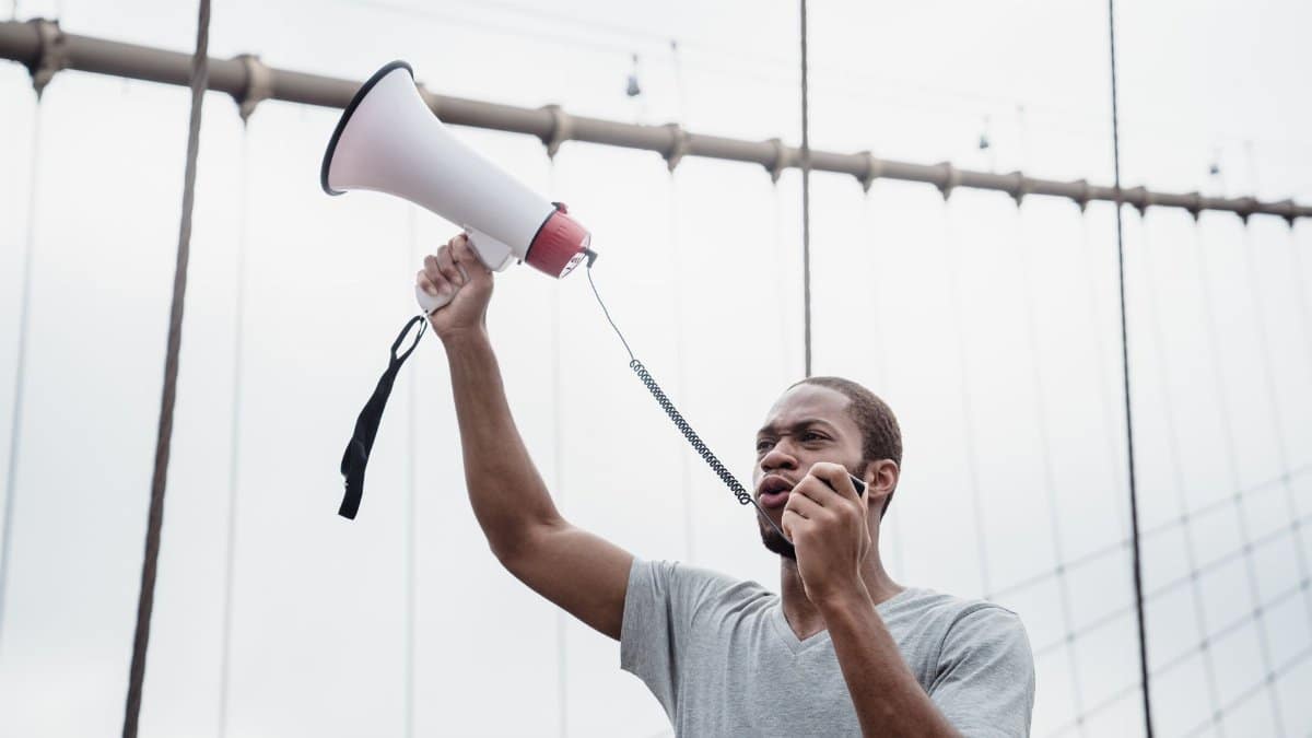 A passionate protester raises a megaphone on a city bridge during a daytime demonstration.