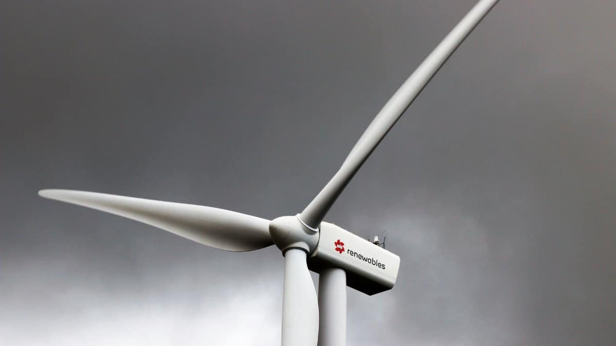 A wind turbine stands tall against dark, cloud-laden skies, symbolizing renewable energy.