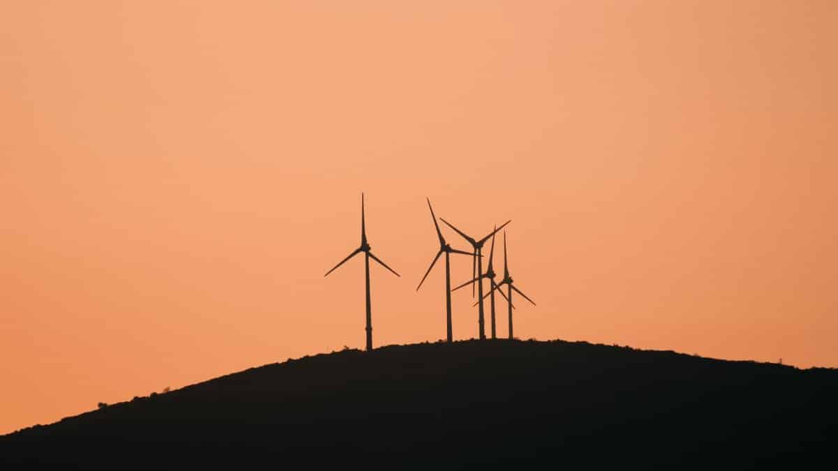 Wind turbines silhouetted against a vibrant yellow sunset sky on a rural hilltop.
