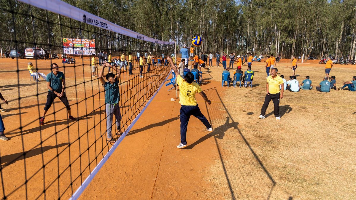 Outdoor volleyball match with diverse teams playing under a clear sky.