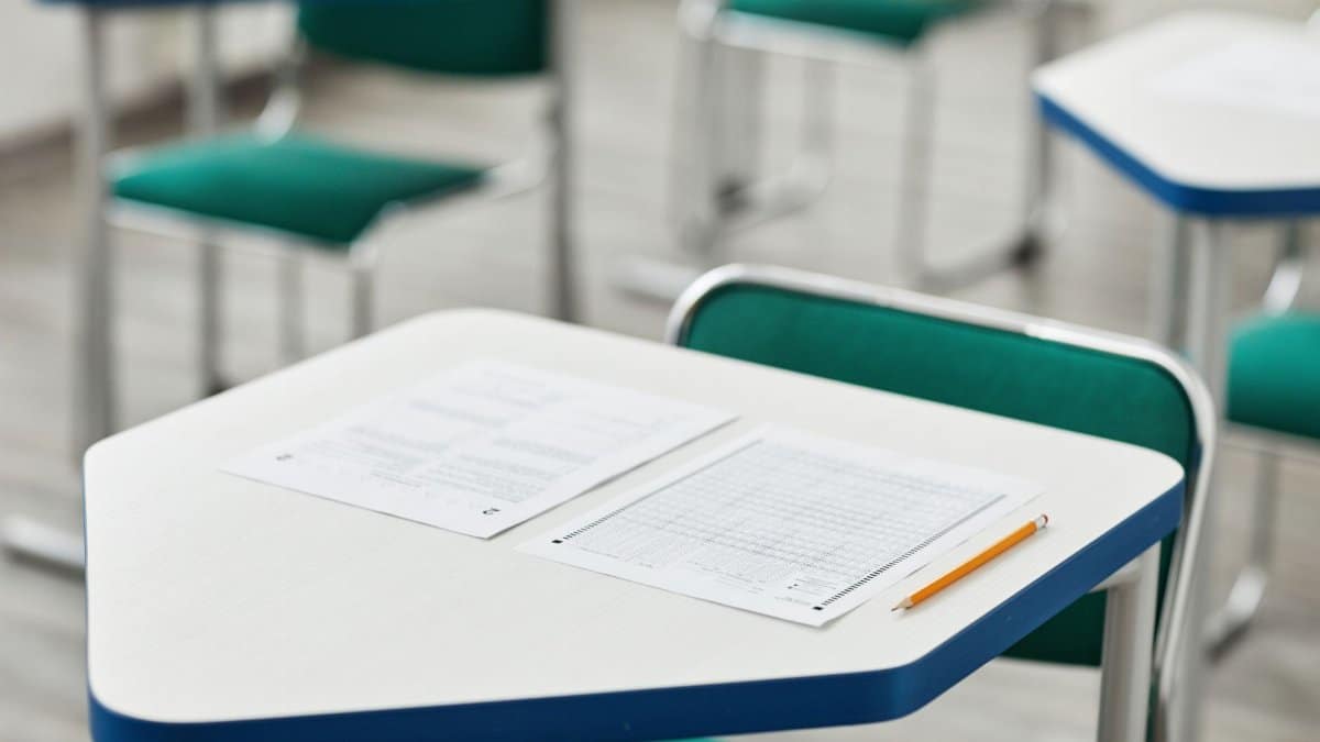 A close-up of an empty classroom desk with exam papers and a pencil, highlighting education and testing environment.