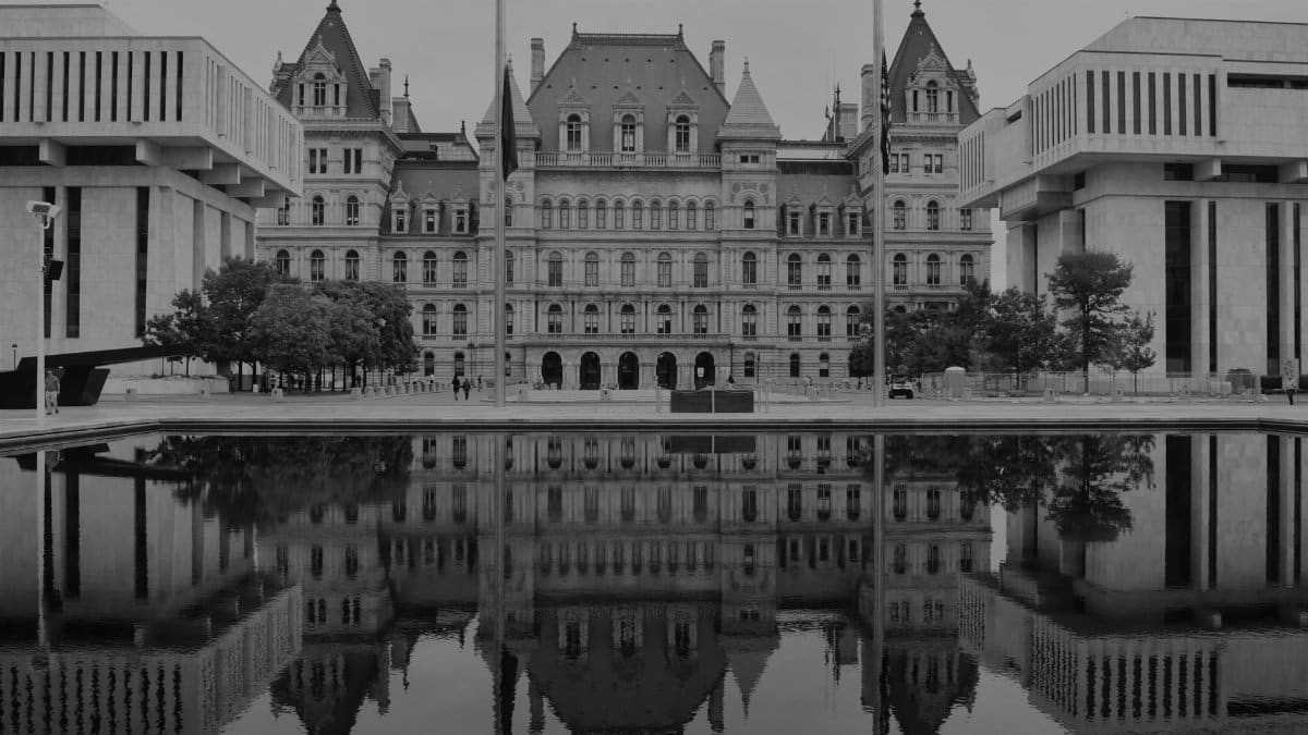 Monochrome photo of the New York State Capitol building with its reflection in water, emphasizing architectural symmetry.
