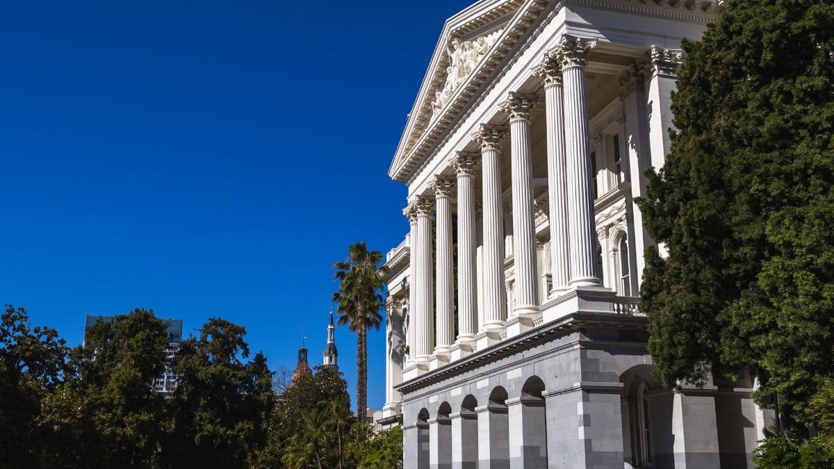 Beautiful sunlit view of the California State Capitol building with classic columns and vibrant blue sky.