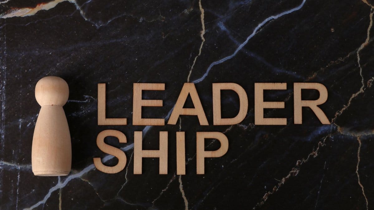 Wooden figure and 'leadership' text on marble surface, representing leadership and guidance.