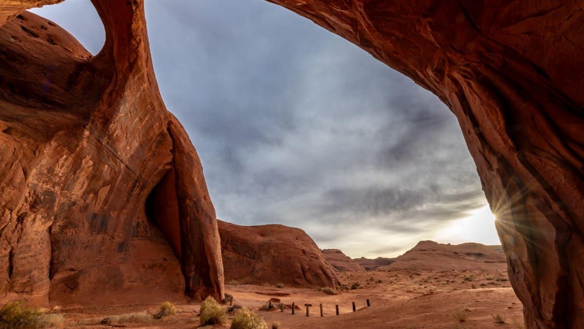 Stunning red rock arch in the desert with sun rays and dramatic clouds creating a breathtaking scene.