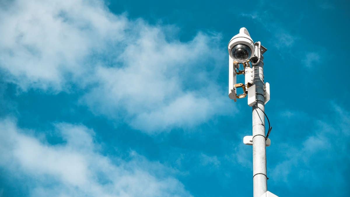 Close-up of a surveillance camera on a pole under a clear blue sky.