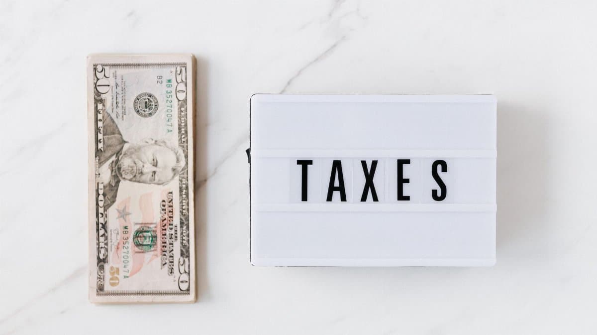 Top view composition of stack of American dollars placed on white marble surface with white retro light box with TAXES inscription