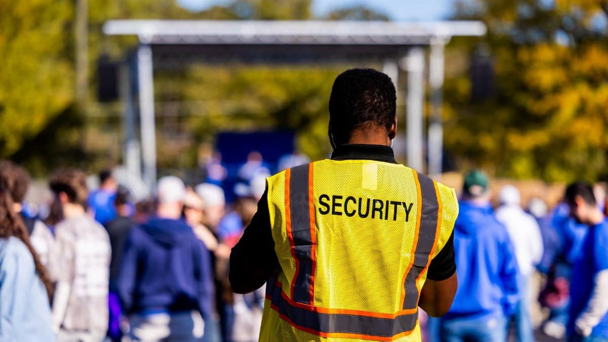 A security guard monitors a crowd at an outdoor event, ensuring safety and order.