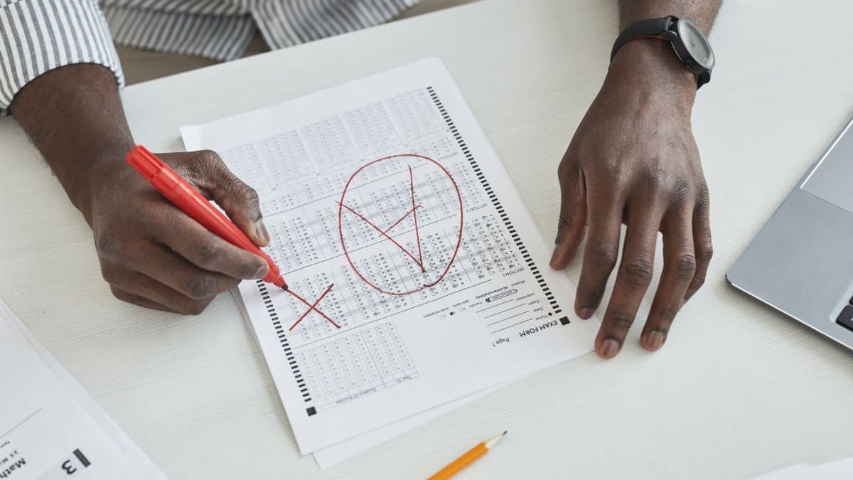 Close-up of a teacher marking a test paper with a red marker on a desk.