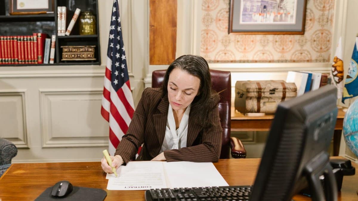 Female attorney in a law office signing legal documents at her desk, surrounded by legal books and symbols of justice.