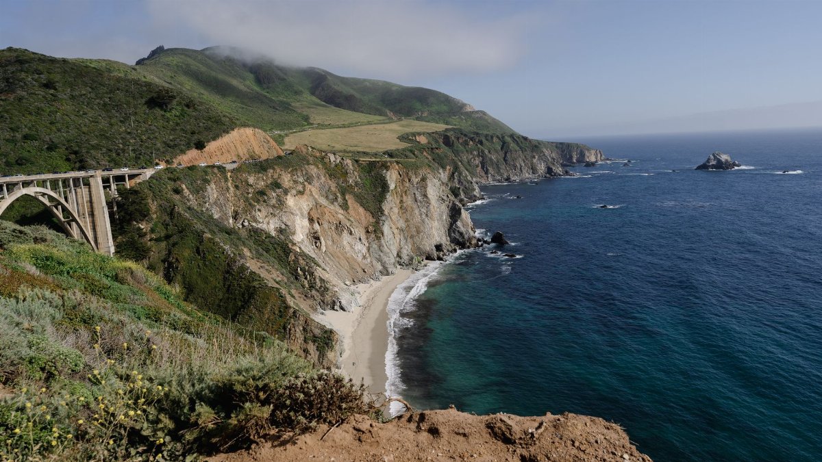 A breathtaking view of a coastal bridge spanning over lush cliffs and azure waters.
