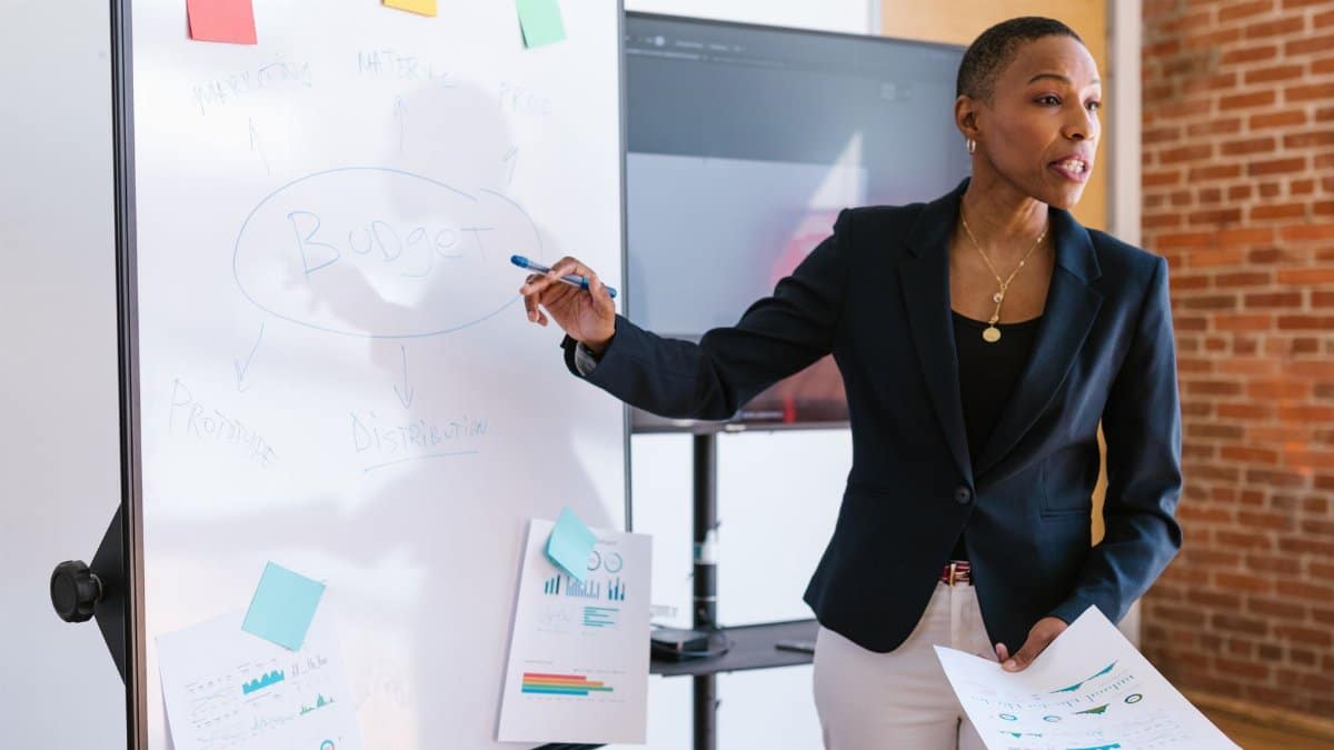Professional businesswoman explaining budget strategy on a whiteboard during a meeting.