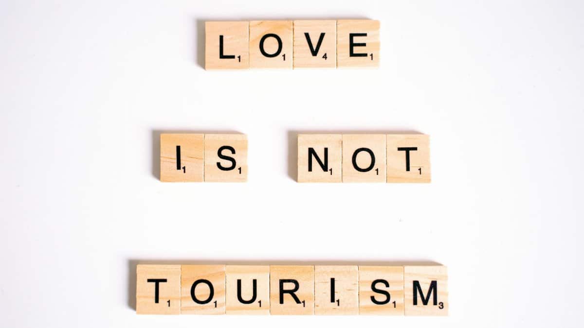 Scrabble tiles spelling 'Love is Not Tourism' on a white surface.