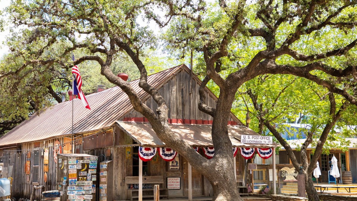 Rustic wooden post office in Luckenbach, Texas, with American flag and oak tree.