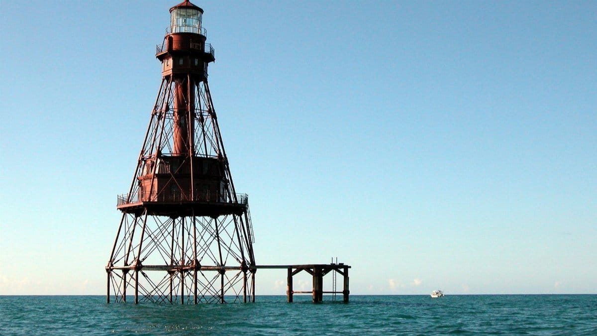 A towering metal lighthouse stands isolated in the ocean under a clear sky.