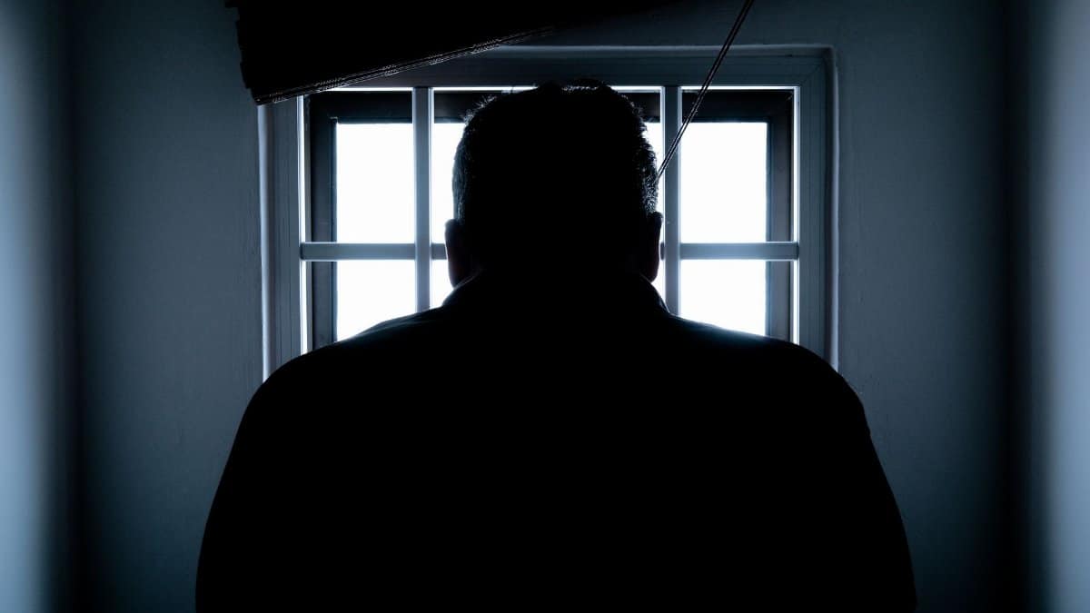 Dark silhouette of a man in a prison cell, backlit by window bars.