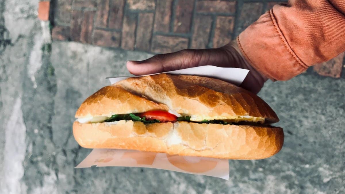 Close-up of a traditional Vietnamese banh mi sandwich held over a street pavement in Hue City, Vietnam.