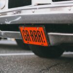 Close-up of a vintage car with a custom orange license plate reading 'GR-RRR!' in a parking lot.