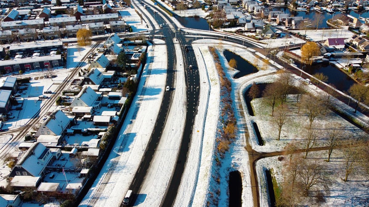 Aerial view of a snowy suburban area with roads, trees, and houses in winter.