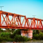 Vibrant red steel bridge spanning a lush green landscape in Pedro Meoqui, Mexico.