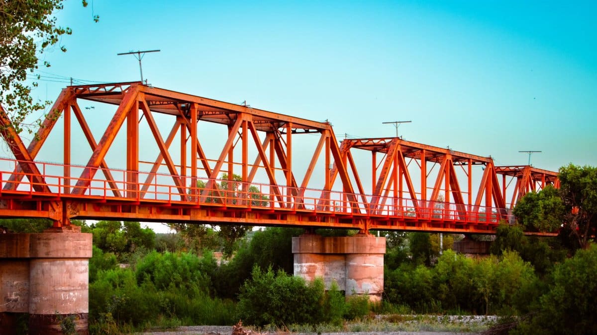 Vibrant red steel bridge spanning a lush green landscape in Pedro Meoqui, Mexico.